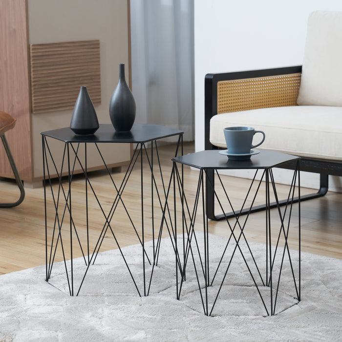 Zwei schwarze Beistelltische mit sechseckigen Tischplatten und filigranen Metallgestellen, dekoriert mit zwei schwarzen Vasen und einer blauen Tasse auf einem hellen Teppich vor einem weißen Sofa