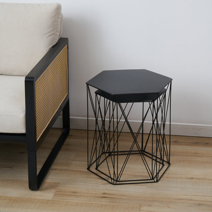Schwarzer Beistelltisch mit sechseckiger Platte und filigranem Metallgestell neben einem Sofa mit schwarzem Holzrahmen und hellen Polstern
