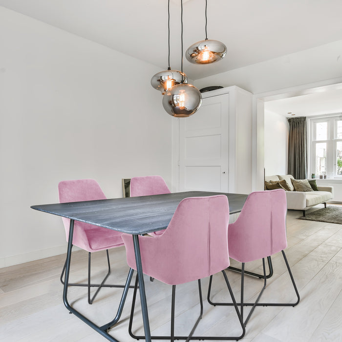 Esszimmer mit rechteckigem dunklem Holztisch und vier rosa Samtstühlen mit Metallgestell, darüber drei runde Hängelampen mit warmem Licht