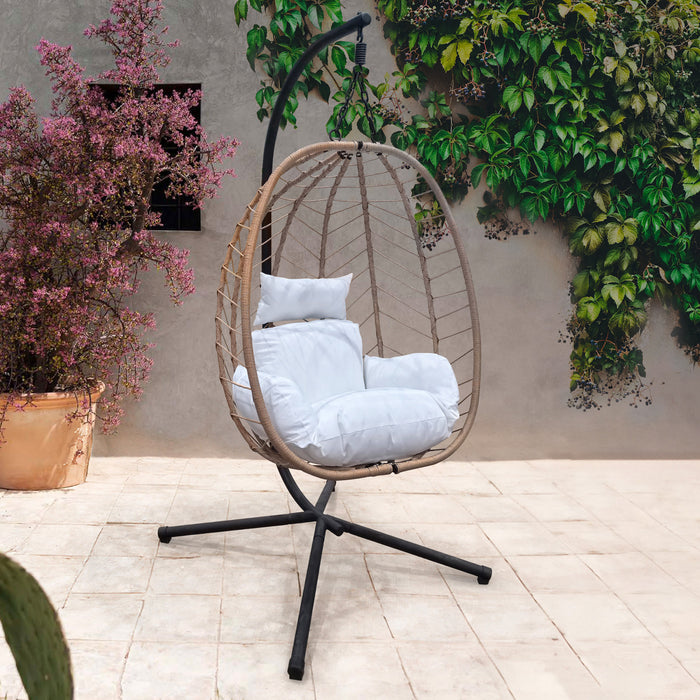 SVITA Shelly Hängesessel in Rattan-Optik mit weißen Kissen auf schwarzem Metallgestell vor Wand mit Kletterpflanzen und Topfpflanze