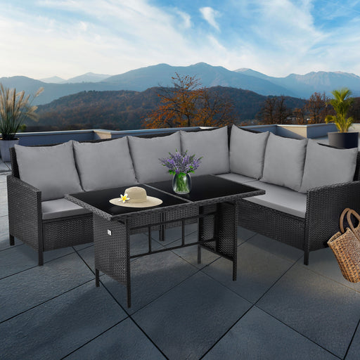 Eckige Gartenlounge mit grauen Kissen und schwarzem Tisch auf Terrasse mit Bergblick, dekoriert mit Vase und Strohhut