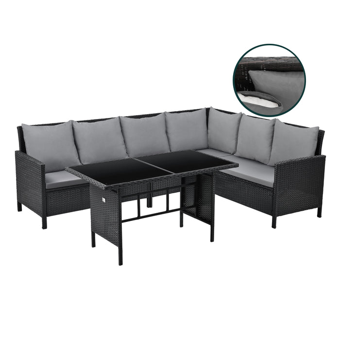 Schwarze Rattan-Ecklounge mit grauen Kissen und Tisch mit Glasplatte