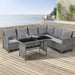 Graues Ecksofa aus Rattan mit grauen Kissen und schwarzem Glastisch auf Holzterrasse mit Meerblick