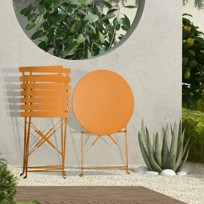 Kleines Metall-Bistro-Set mit rundem Tisch und zwei Klappstühlen in orange steht zusammengeklappt auf einer Terrasse