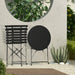 Kleines Metall-Bistro-Set mit rundem Tisch und zwei Klappstühlen in schwarz steht zusammengeklappt auf einer Terrasse