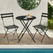 Kleines Metall-Bistro-Set mit rundem Tisch und zwei Klappstühlen in schwarz steht an einem Pool