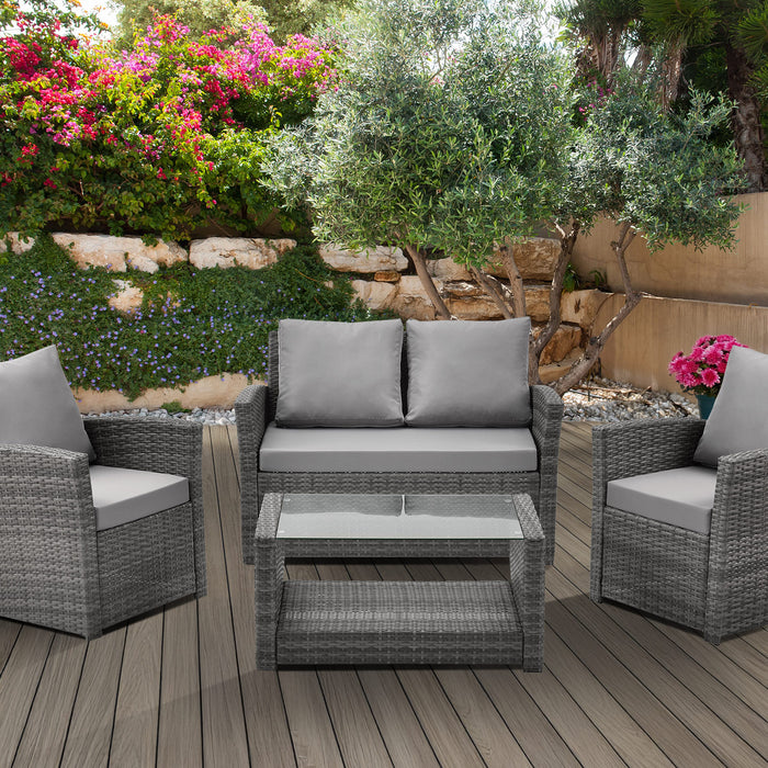 Gartenmöbel-Set aus grauem Polyrattan mit zwei Sesseln, einem Sofa und einem Glastisch mit Ablage auf einer Terrasse