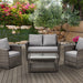 Gartenmöbel-Set aus braunem Polyrattan mit zwei Sesseln, einem Sofa und einem Glastisch mit Ablage auf einer Terrasse
