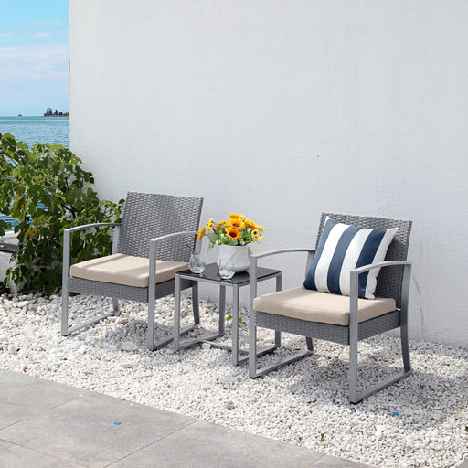 Zwei graue Gartenstühle mit hellen Sitzkissen und ein kleiner Tisch mit Sonnenblumen auf weißem Kies vor einer weißen Wand und Blick auf Wasser