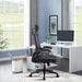 Schwarzer ergonomischer Bürostuhl mit Kopfstütze vor einem weißen Schreibtisch mit Computer in hellem Arbeitszimmer mit großen Fenstern und blauen Wänden