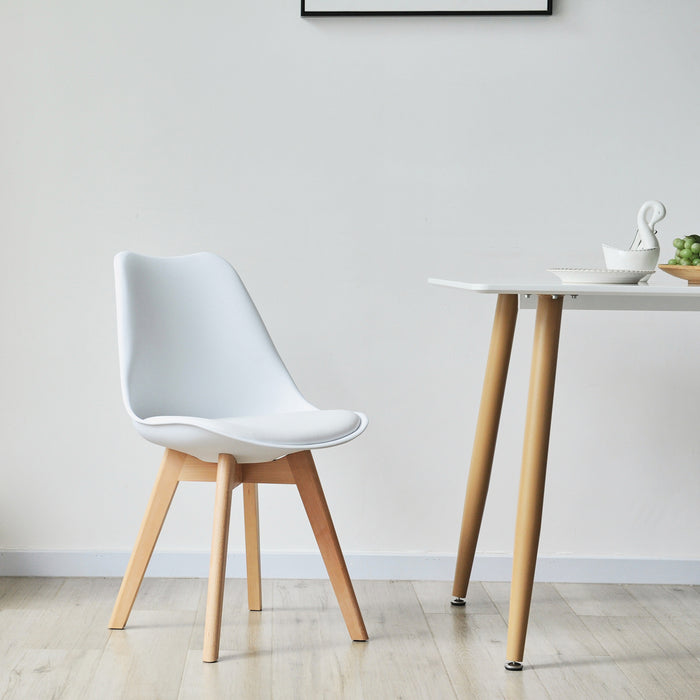 Weißer SVITA Mats Esszimmerstuhl mit elegantem Design neben einem weißen Tisch mit Holzbeinen in einem minimalistischen Raum