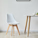 Weißer SVITA Mats Esszimmerstuhl mit elegantem Design neben einem weißen Tisch mit Holzbeinen in einem minimalistischen Raum