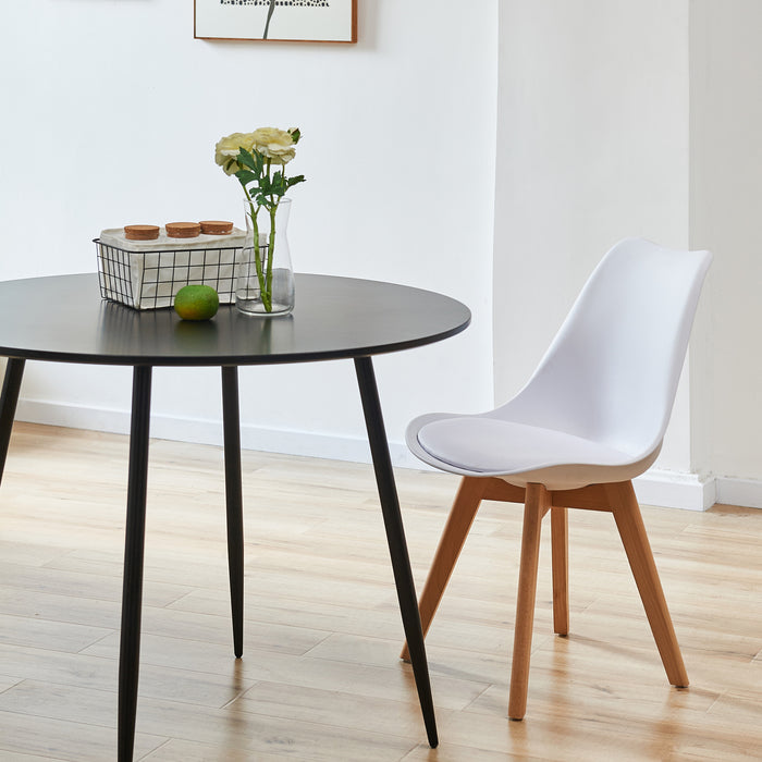 Bequemer SVITA Mats Esszimmerstuhl in Weiß mit Holzbeinen neben rundem schwarzem Tisch mit Blumenvase und Obst