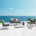 Moderner Sitzbereich mit grauen Polstersesseln und Sofa, grüne Kissen, Glastisch auf weißer Terrasse mit Meerblick