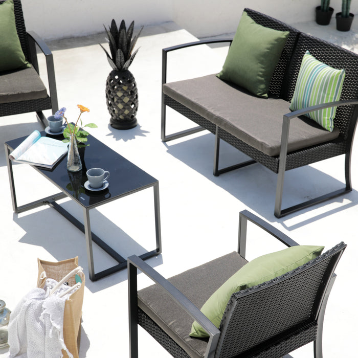 Moderner Außenbereich mit schwarzem Rattan-Loungeset, grünen Kissen und einem schwarzen Glastisch mit Tassen und einer Vase mit Blume