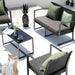 Moderner Außenbereich mit schwarzem Rattan-Loungeset, grünen Kissen und einem schwarzen Glastisch mit Tassen und einer Vase mit Blume