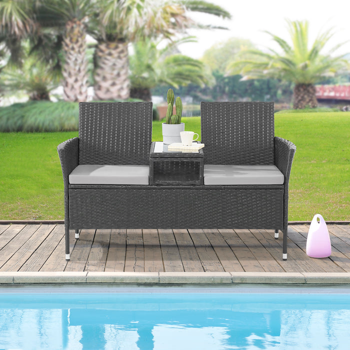 Zweisitzige Gartenbank aus schwarzem Rattan mit zwei grauen Sitzkissen und integriertem Tisch mit Glasplatte in der Mitte steht an einem Pool