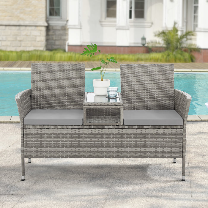 Zweisitzige Gartenbank aus grauem Rattan mit zwei grauen Sitzkissen und integriertem Tisch mit Glasplatte in der Mitte vor einem Pool