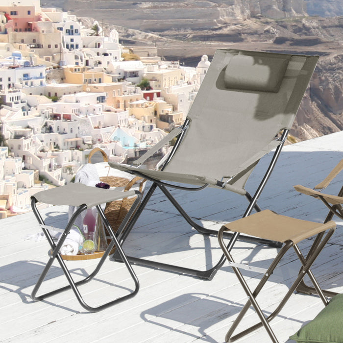 Grauer Klappstuhl mit Kopfstütze und zwei kleine Klapphocker auf einer Terrasse mit Blick auf weiße Häuser an einem Hang