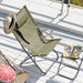 Grüner Klappstuhl mit Strohhut auf einer weißen Terrasse, daneben kleiner Klapphocker mit aufgeschlagenem Magazin