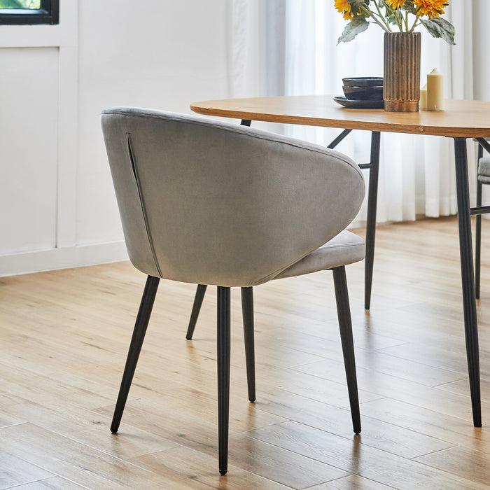 Rückansicht des grauen SVITA Audrey Esszimmerstuhls mit schwarzem Metallgestell neben einem Holztisch mit schwarzen Beinen und einer Vase mit Sonnenblumen