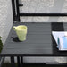 Schwarzer Metalltisch mit gelber Tasse und aufgeschlagenem Magazin bei Sonnenlicht