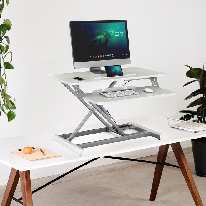 Weißer höhenverstellbarer Schreibtischaufsatz voll ausgefahren mit Computer, Tastatur und Maus auf weißem Tisch mit Holzbeinen