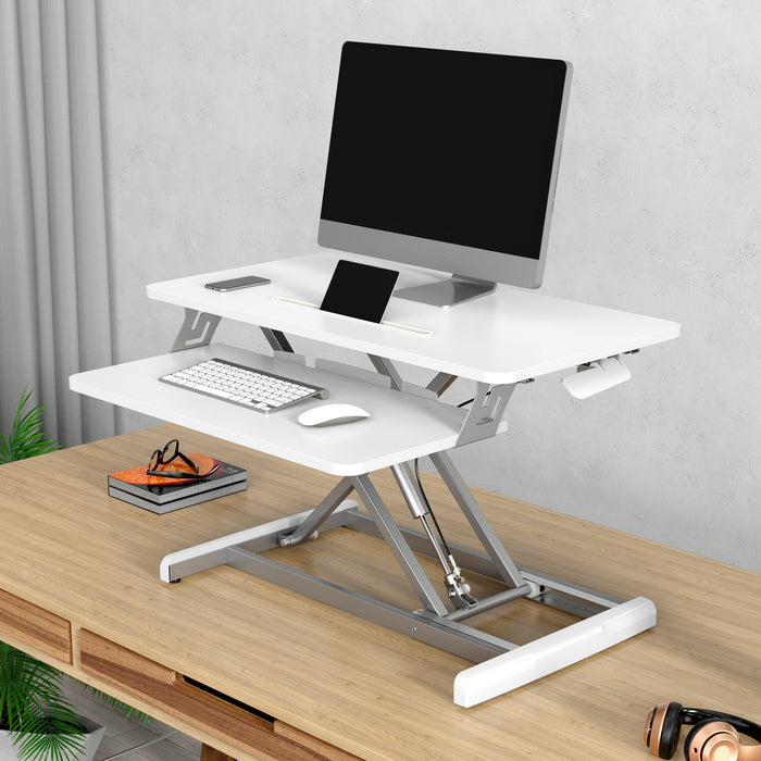 Weißer höhenverstellbarer Schreibtischaufsatz mit Monitor, Tastatur und Maus auf einem hellen Holztisch