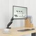 Schwenkbarer Monitorarm mit Bildschirm über einem Schreibtisch mit Tastatur, Maus, Tasse und Holz-Organizer