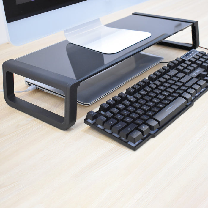 Schwarze Monitorerhöhung aus Kunststoff auf einem Schreibtisch mit einem Laptop darunter und einer schwarzen Tastatur davor