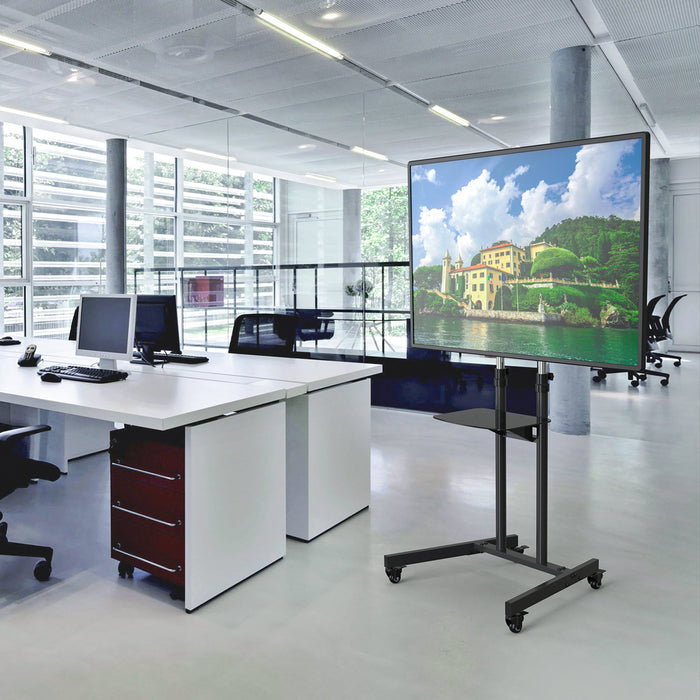 Moderner Büroarbeitsplatz mit weißen Schreibtischen und Computern, daneben ein mobiler TV-Ständer mit einem Bildschirm, der eine Landschaft mit Häusern und Wasser zeigt