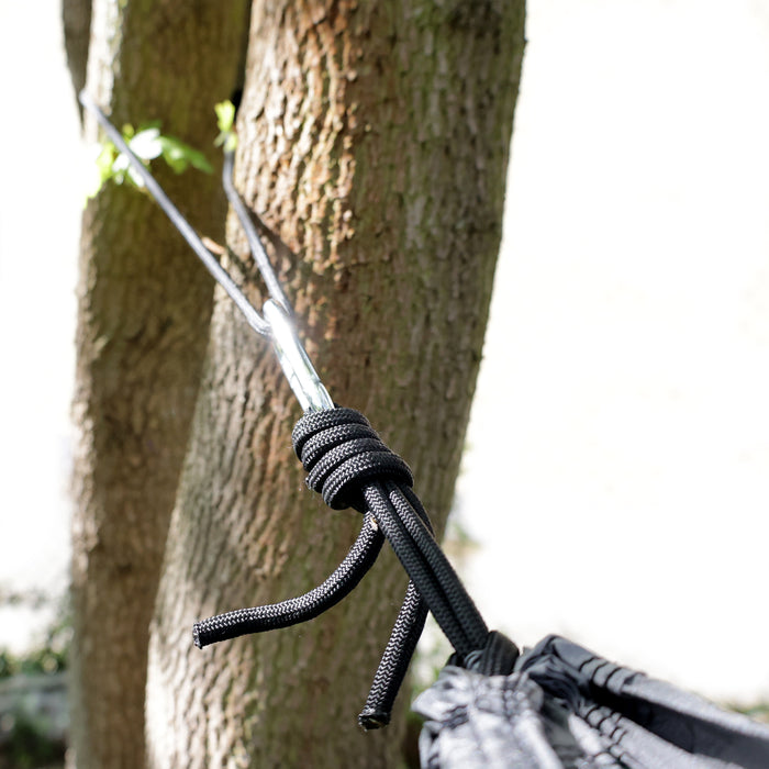Schwarzes Seil mit Knoten und Karabinerhaken, befestigt an einem Baumstamm im Freien