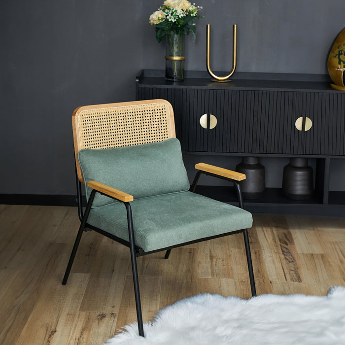 Grüner Loungestuhl mit Rattan-Rückenlehne und Holzarmlehnen vor schwarzem Sideboard mit goldfarbenen Griffen
