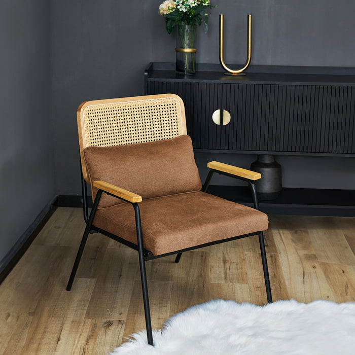 Brauner Loungestuhl mit Rattan-Rückenlehne und Holzarmlehnen vor schwarzem Sideboard mit goldfarbenen Griffen