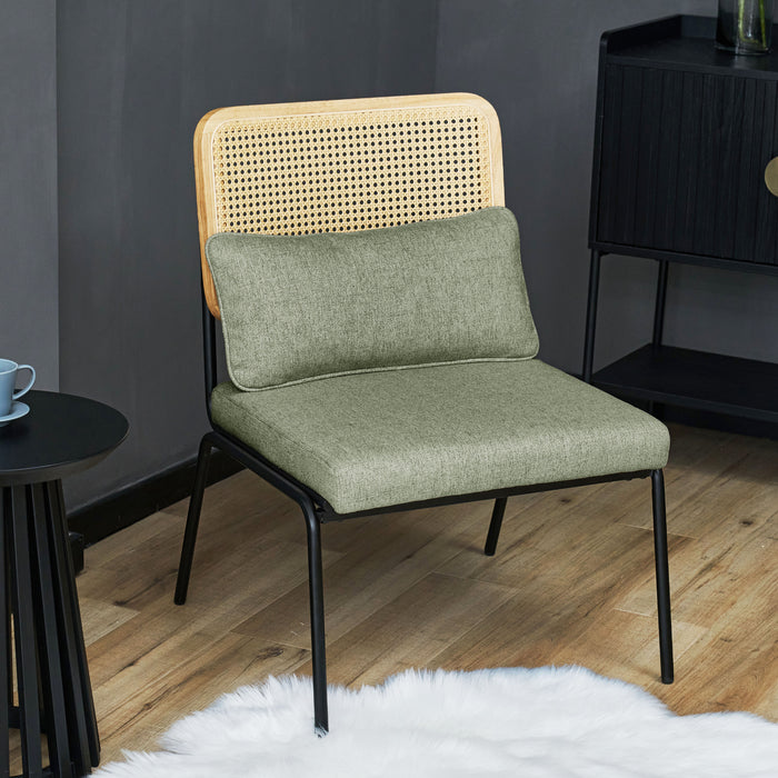 Grüner Loungesessel mit Rattanlehne und schwarzem Metallgestell auf Holzboden vor dunkler Wand