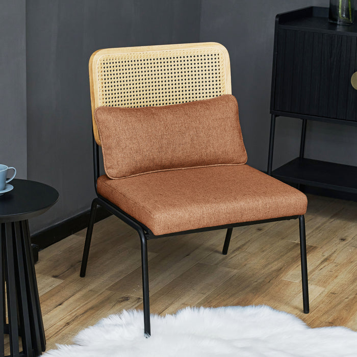 Brauner Loungesessel mit Rattanlehne und schwarzem Metallgestell auf Holzboden vor dunkler Wand