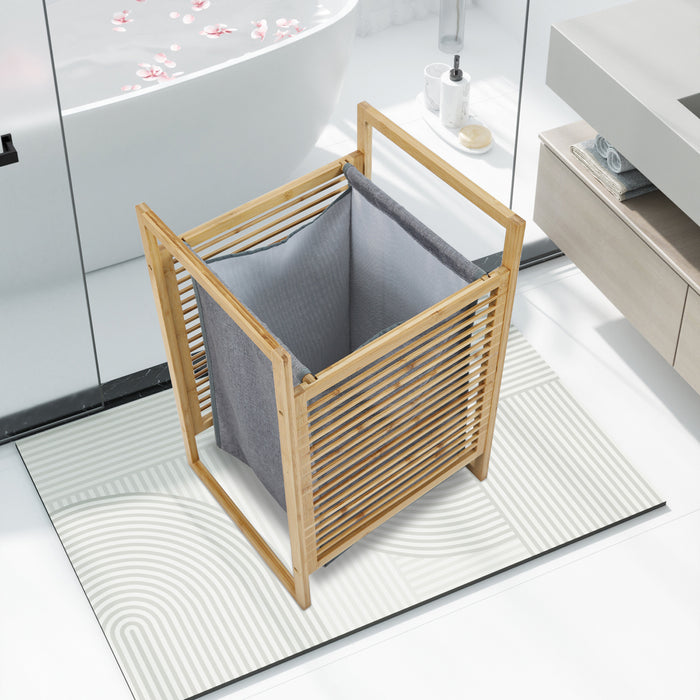 Moderner Wäschekorb aus Holz mit grauem Stoffeinsatz steht auf einem weißen Badezimmerteppich neben Badewanne und Waschbecken