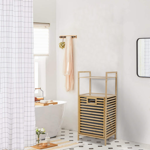 Ein Bambus Badregal mit Wäschekorb steht in einem hellen Badezimmer mit freistehender Badewanne mit weißem Duschvorhang mit Karomuster und rechteckigem Spiegel an der Wand