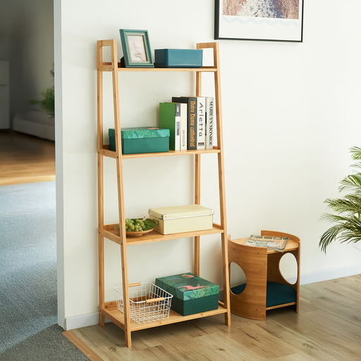 Offenes, vierstufiges Regal aus hellem Holz mit Büchern, grünen Boxen und Dekoration in einem hellen Raum neben einem kleinen runden Beistelltisch
