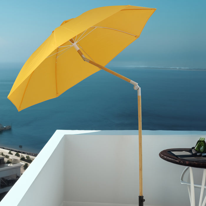 Gelber Sonnenschirm mit Holzstiel auf weißem Balkon mit Blick auf das blaue Meer