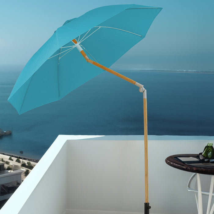 Blauer Sonnenschirm mit Holzstiel auf weißem Balkon mit Blick auf das Meer und einen kleinen runden Tisch mit grünem Getränk