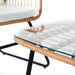 Nahaufnahme Glasplatte auf einem Tisch mit geflochtenem Rand aus Rattan und schwarzem Metallgestell, daneben Teil eines Stuhls mit weißem Polster und Rattanrahmen