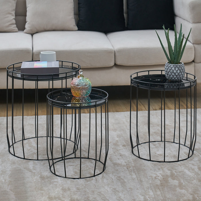 Drei schwarze Metall-Beistelltische mit runden Tischplatten, dekoriert mit Buch, Tasse, bunter Glasflasche und Aloe-Pflanze vor beigem Sofa